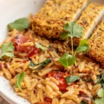 Cremiger Tomaten-Orzo mit knusprigen Tofu-Cutlets auf einem Teller.