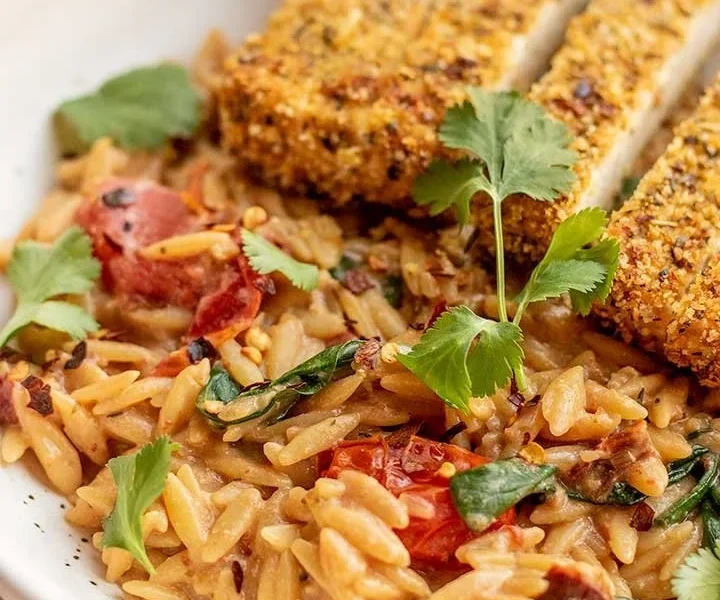 Cremiger Tomaten-Orzo mit knusprigen Tofu-Cutlets auf einem Teller.