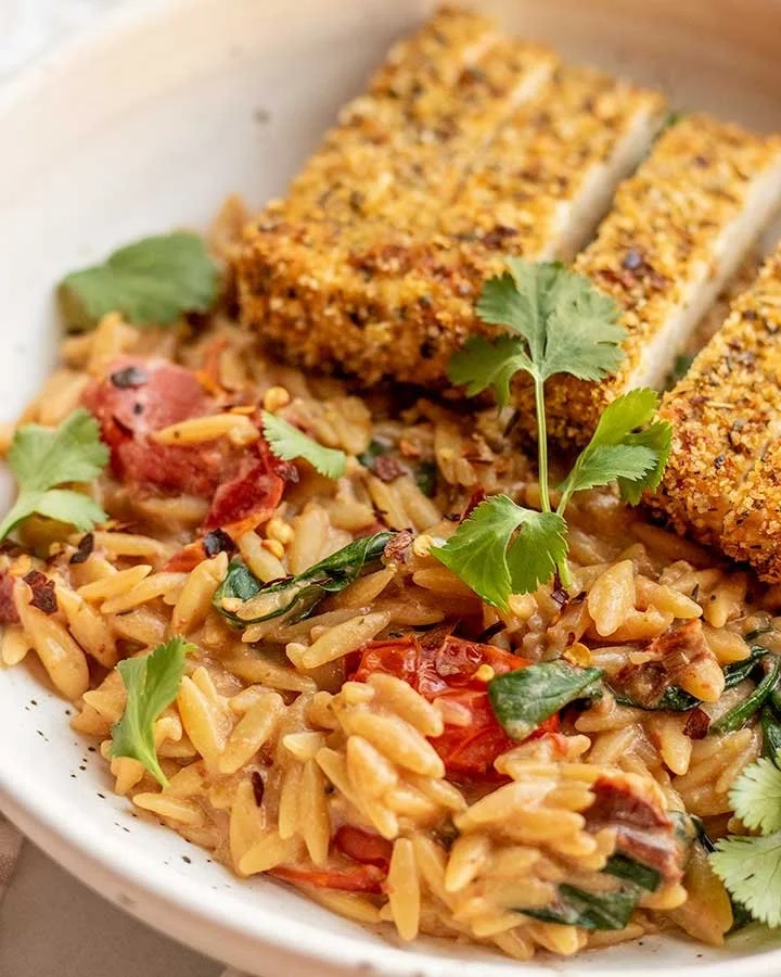 Cremiger Tomaten-Orzo mit knusprigen Tofu-Cutlets auf einem Teller.