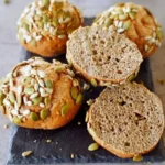 Eiweißbrötchen aus roten Linsen auf einem Holzbrett präsentiert.