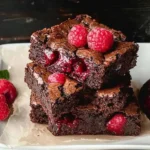 Himbeer-Brownies in einer Schüssel, mit frischen Himbeeren und Schokolade garniert.