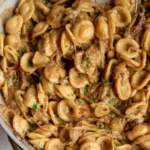 Karamellisierte Zwiebel-Pasta in einer Schüssel mit frischen Kräutern garniert.
