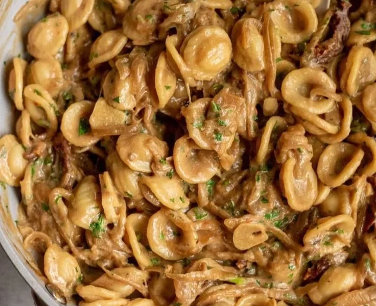 Karamellisierte Zwiebel-Pasta in einer Schüssel mit frischen Kräutern garniert.