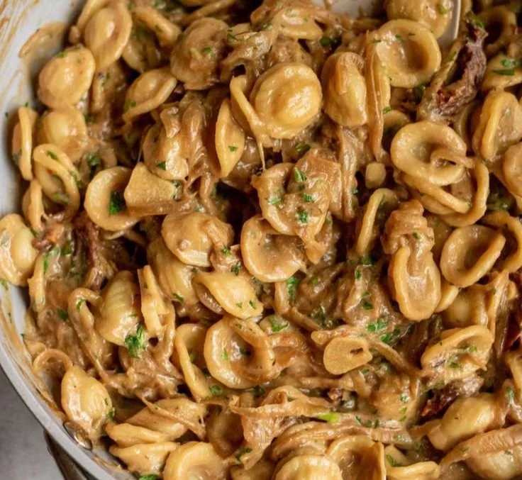 Karamellisierte Zwiebel-Pasta in einer Schüssel mit frischen Kräutern garniert.