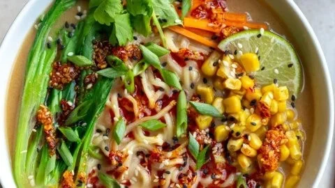 Schale mit Peanut Butter Miso Ramen, garniert mit frischem Gemüse und Kräutern.