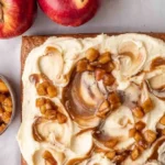 Veganer Apfelmus-Kuchen auf einem weißen Teller, garniert mit frischen Äpfeln.
