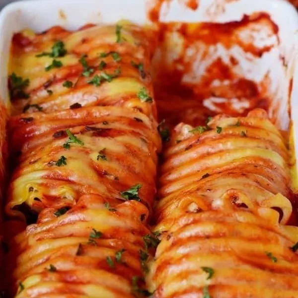 Vegane Lasagne Rollen auf einem Teller, serviert mit frischen Kräutern.