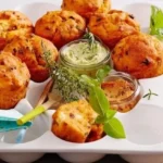 Vegane Pizza-Muffins auf einem Holzbrett, mit frischen Kräutern garniert.