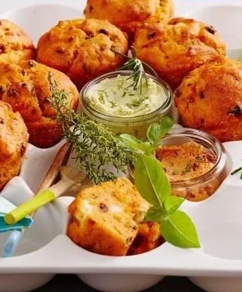 Vegane Pizza-Muffins auf einem Holzbrett, mit frischen Kräutern garniert.
