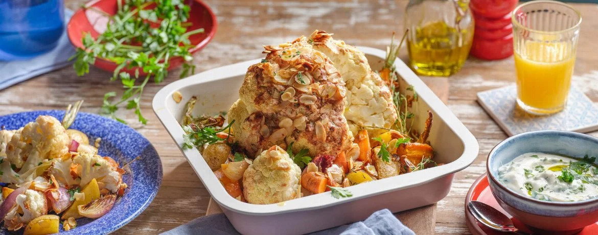 Ganzer Blumenkohl mit Ofengemüse und Kräuter-Dip auf einem Teller