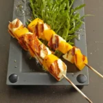 Mango-Halloumi-Spiesschen auf Rucolasalat garniert und angerichtet.