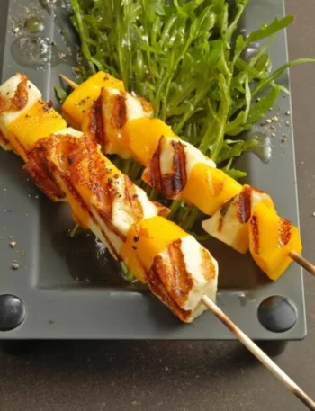 Mango-Halloumi-Spiesschen auf Rucolasalat garniert und angerichtet.