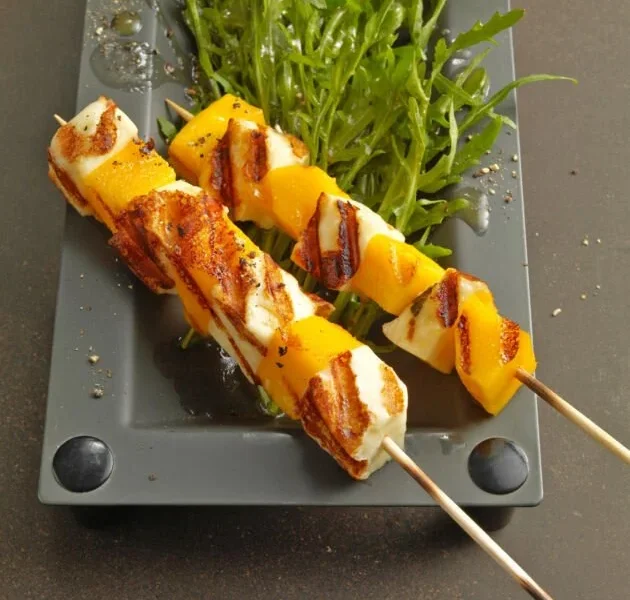 Mango-Halloumi-Spiesschen auf Rucolasalat garniert und angerichtet.