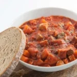 Veganes Gulasch mit Räuchertofu und Kartoffeln auf einem Teller angerichtet.