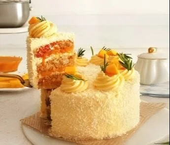 Veganer Mango-Kokosnusskuchen auf einem Teller, dekoriert mit Mangostückchen.