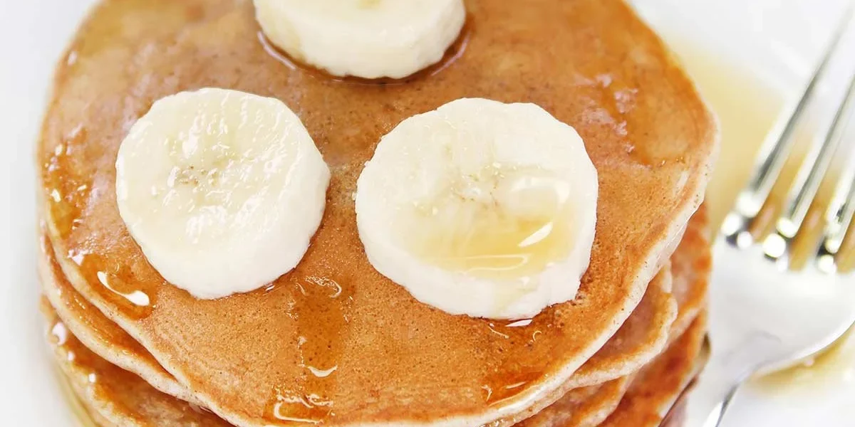 Vegane Bananenpfannkuchen auf einem Teller, dekoriert mit frischen Bananen und Sirup.