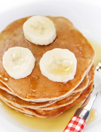 Vegane Bananenpfannkuchen auf einem Teller, dekoriert mit frischen Bananen und Sirup.