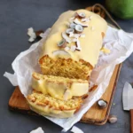 Einfacher Mango Kokosnuss Kastenkuchen auf einem Teller, dekoriert mit frischen Mangostücken.