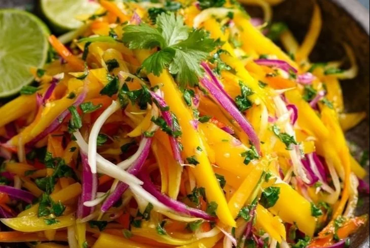 Bunte Schüssel mit Mango Slaw, garniert mit frischen Kräutern und Limetten.
