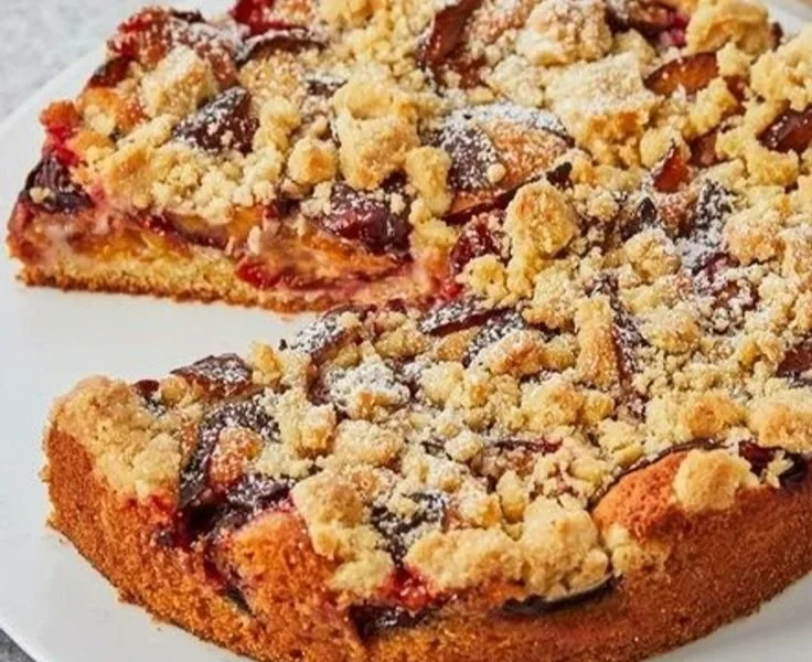 Pflaumenkuchen mit Streuseln auf einem Teller, frisch gebacken und verziert