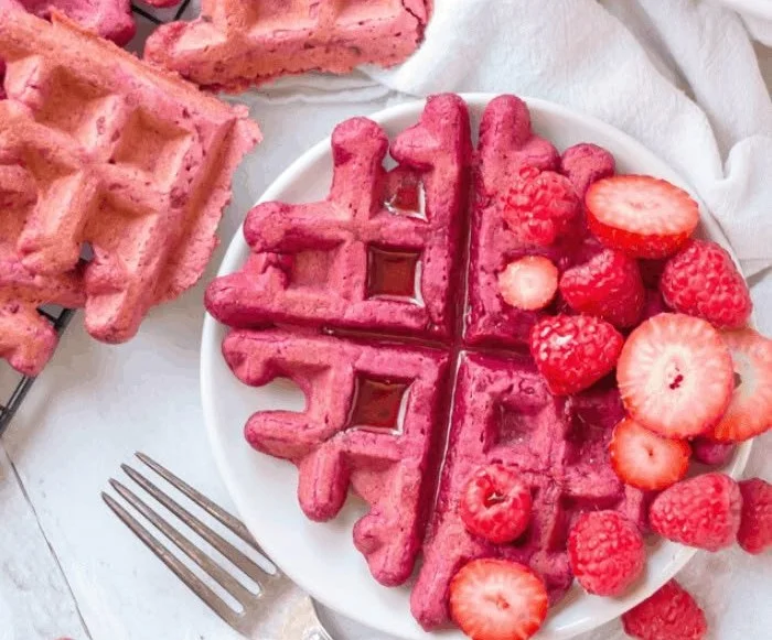 Vegane Rote Beete Waffeln auf einem Teller, dekoriert mit frischen Früchten.