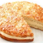 Veganer Bienenstich auf einem Kuchenteller, dekoriert mit Mandeln und Sahne.