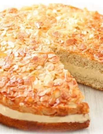Veganer Bienenstich auf einem Kuchenteller, dekoriert mit Mandeln und Sahne.
