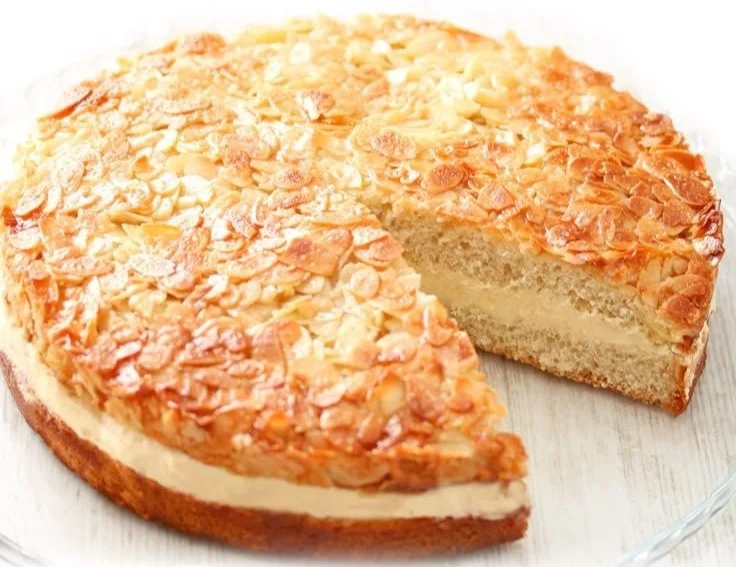 Veganer Bienenstich auf einem Kuchenteller, dekoriert mit Mandeln und Sahne.