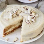 Veganer Kokosnusskuchen auf einem Holzbrett mit Kokosraspeln dekoriert.