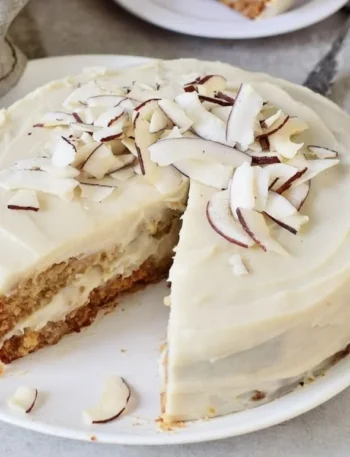 Veganer Kokosnusskuchen auf einem Holzbrett mit Kokosraspeln dekoriert.