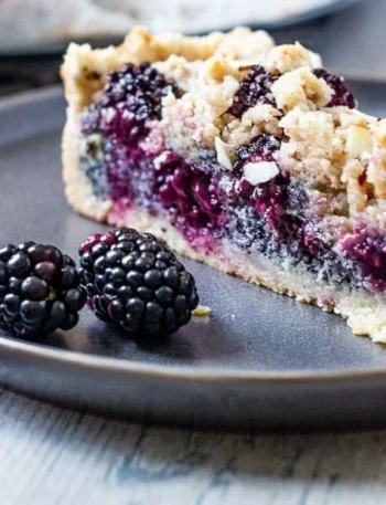Veganer Streuselkuchen mit Brombeeren und Mohn auf einem Tisch serviert.