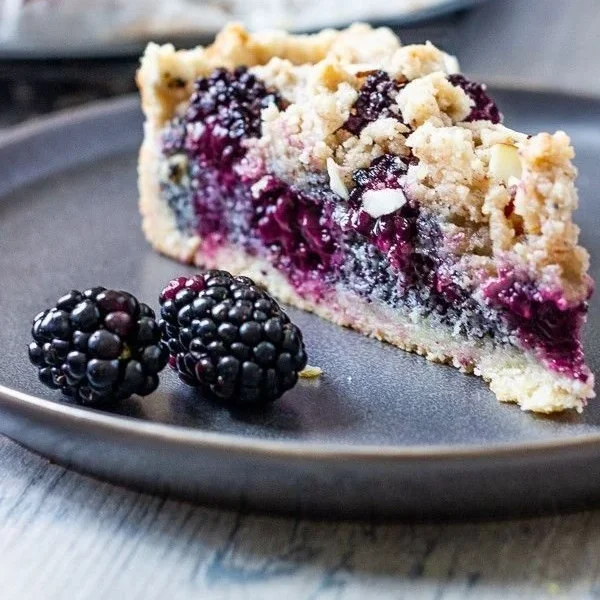 Veganer Streuselkuchen mit Brombeeren und Mohn auf einem Tisch serviert.