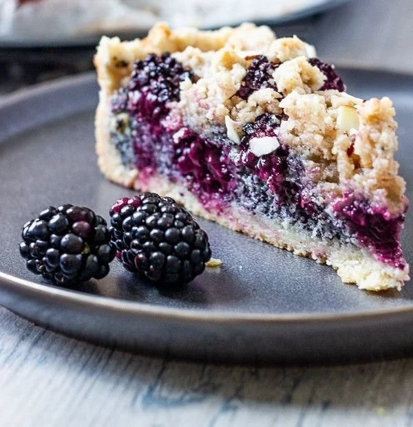 Veganer Streuselkuchen mit Brombeeren und Mohn auf einem Tisch serviert.