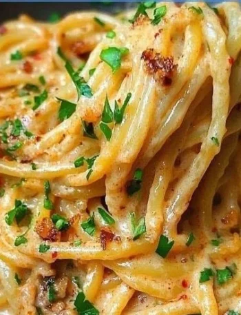Cremige vegane Pasta mit karamellisierten Zwiebeln auf einem Teller serviert.