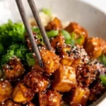 Knuspriger gebackener Sesam-Tofu auf einem Teller mit frischen Kräutern