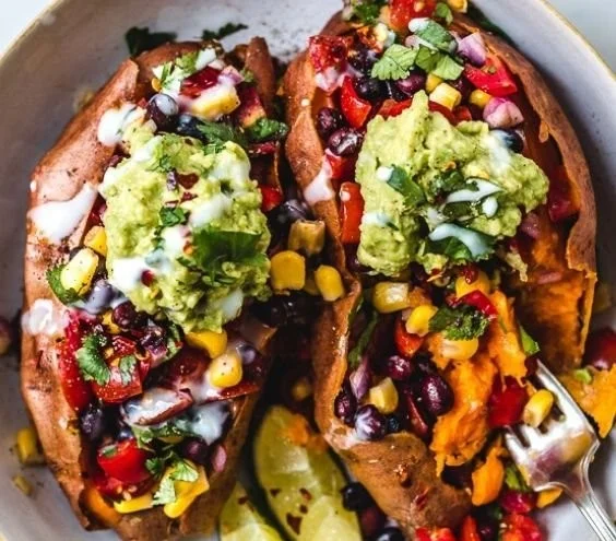 Vegane gefüllte Süßkartoffeln mit buntem Gemüse und Kräutern auf einem Teller.