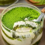 Veganer Matcha Tiramisu auf einem Teller mit grünem Matcha-Pulver dekoriert.