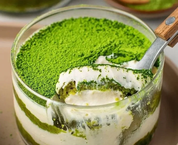 Veganer Matcha Tiramisu auf einem Teller mit grünem Matcha-Pulver dekoriert.